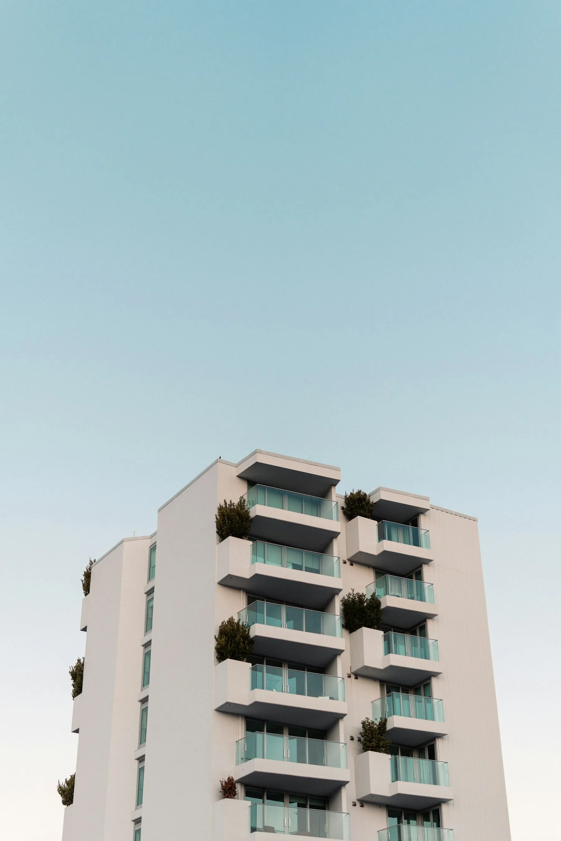 Fachada branca do Alto da Maré, com varandas de vidro e plantas, contra o céu azul